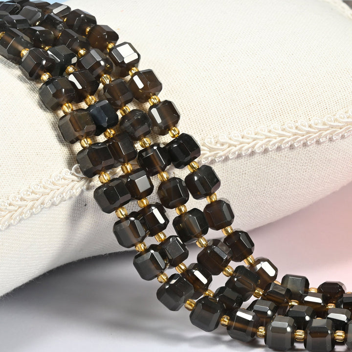 Ice obsidian faceted cube beads 8mm with small gold spacer beads, several strands draped over a cream cushion with braided trim
