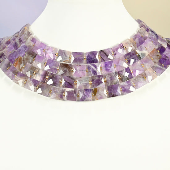 Natural amethyst faceted flat square strands arranged as a layered collar on a white display bust, purple beads across the neck