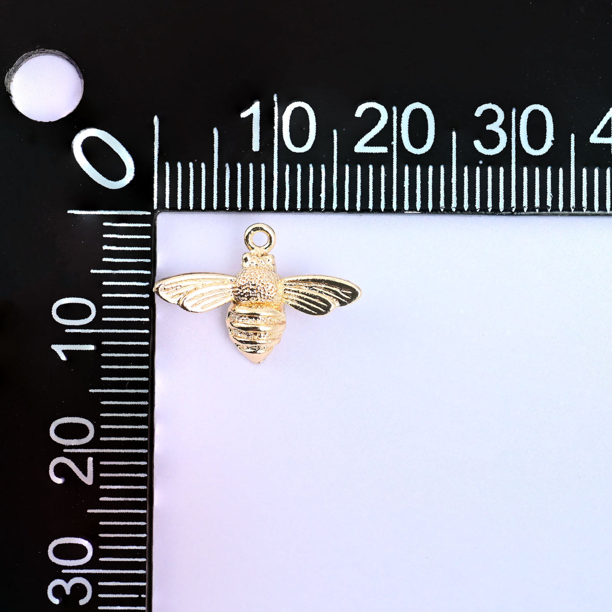 Small gold charms bee measured against a millimeter ruler showing the 17mm wingspan