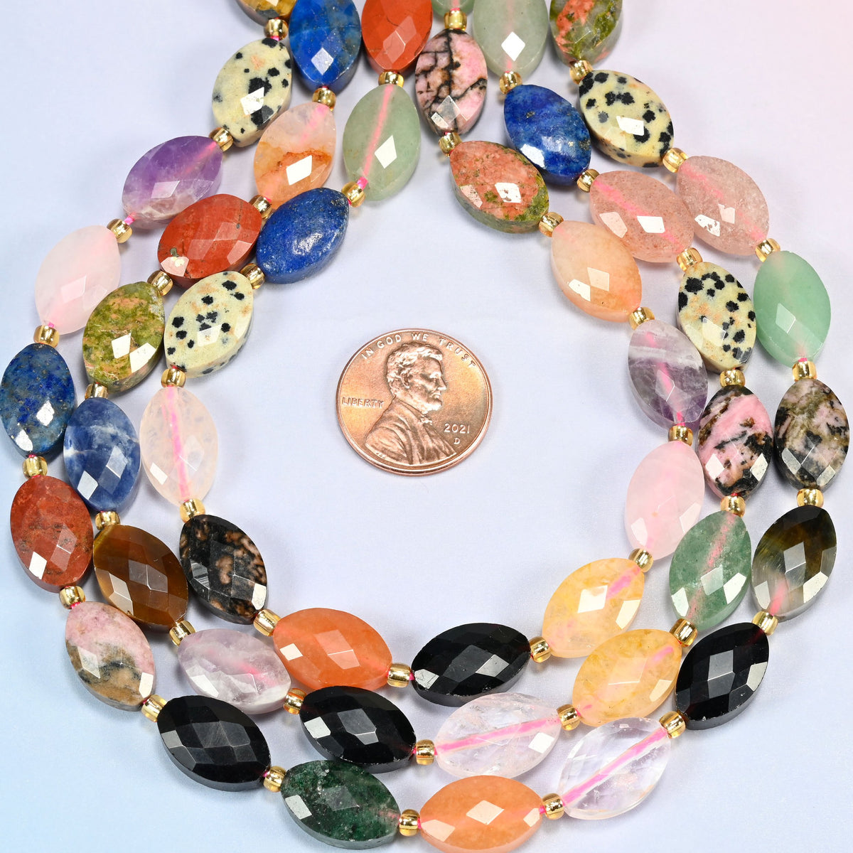 Assorted gemstone faceted flat oval strands formed into a teardrop loop around a US penny for scale