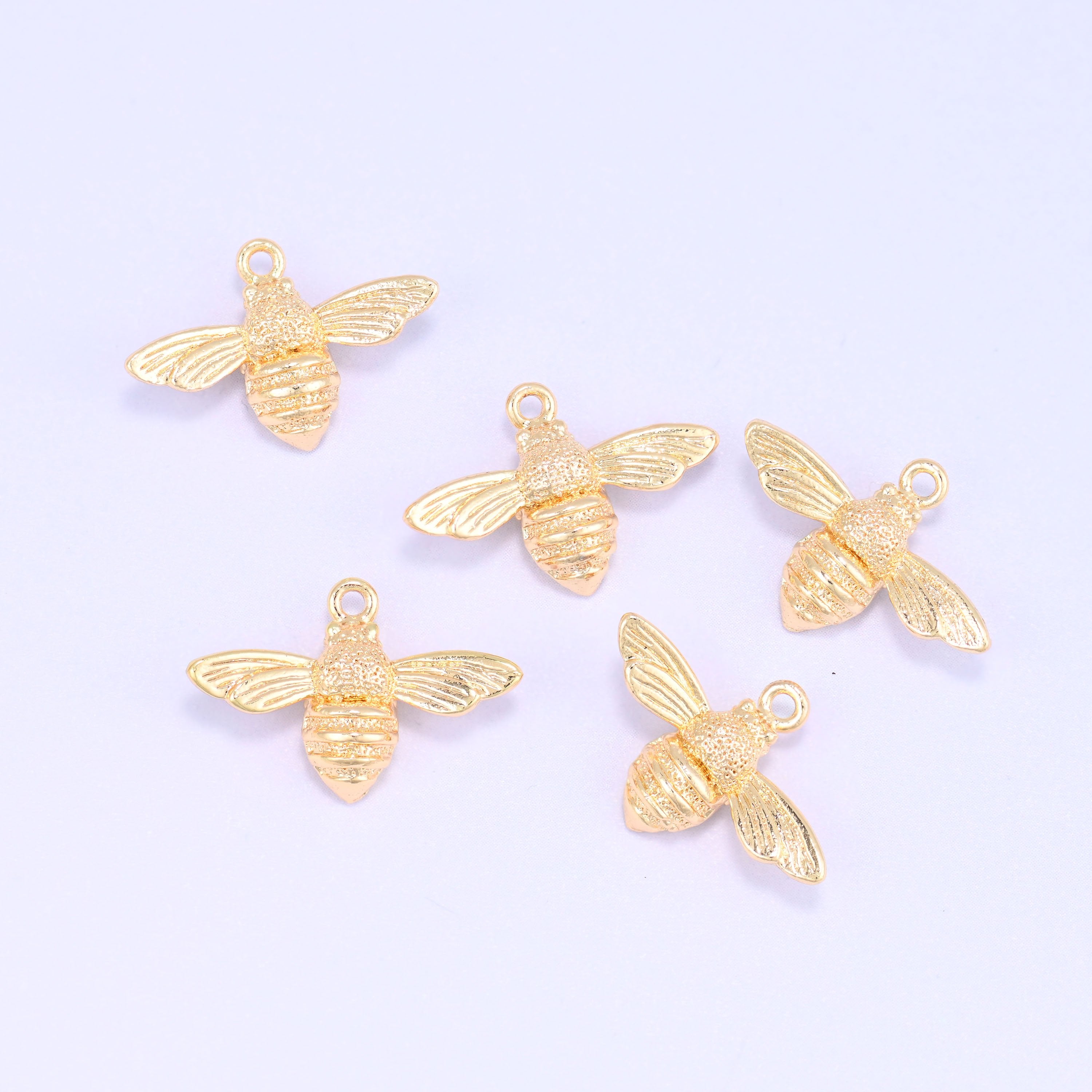 Small gold charms bee, five 18K gold plated bee charms grouped together on a lilac backdrop