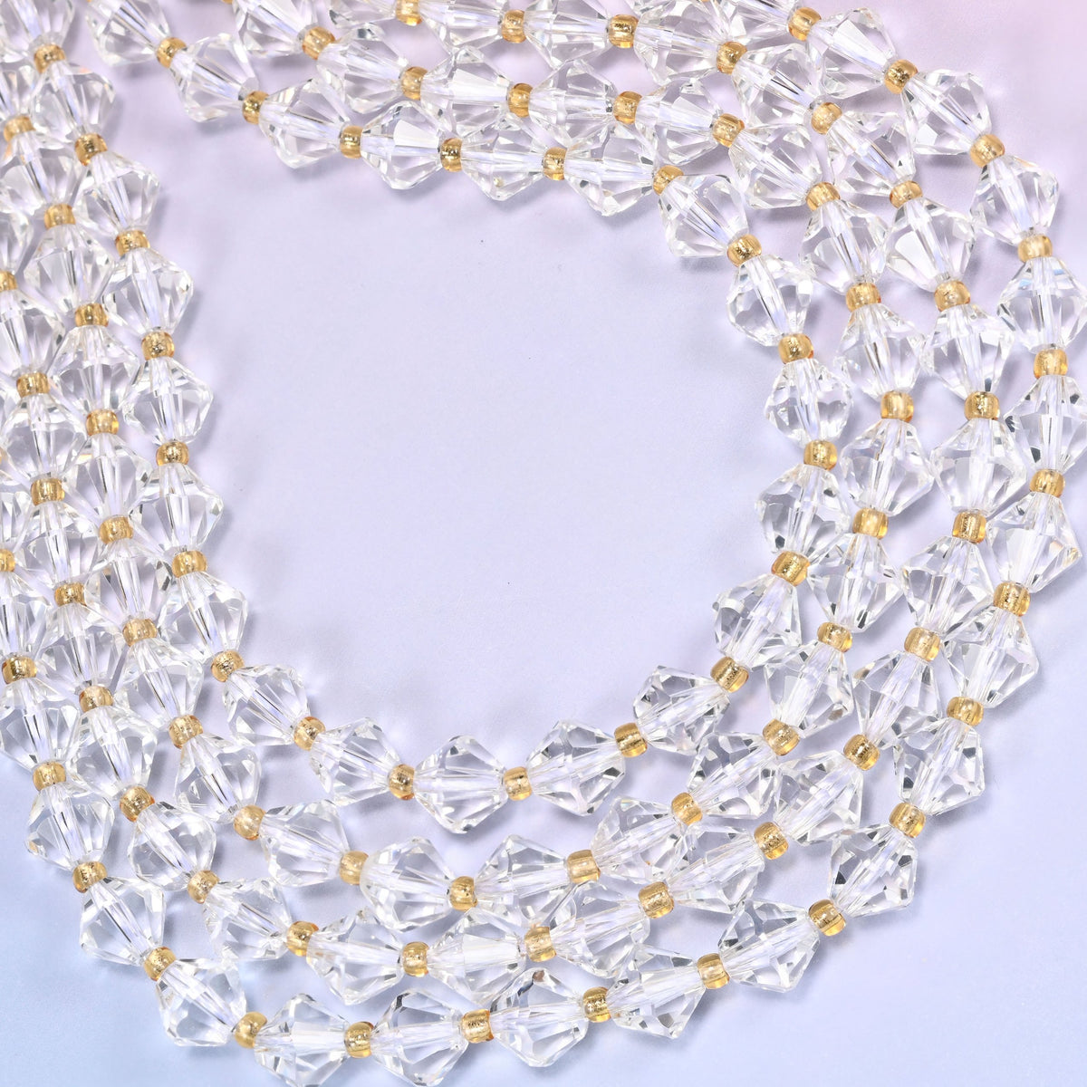8mm Clear Quartz faceted bicone beads coiled into a loose circle on a light lavender background.