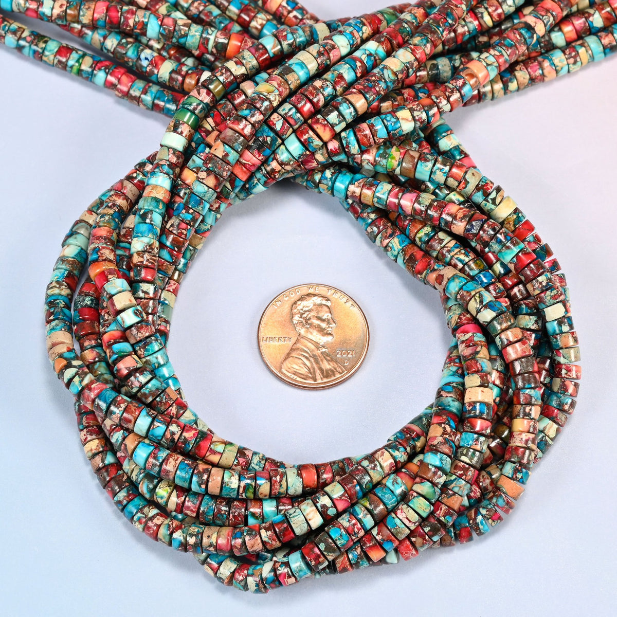 Dyed red blue sea sediment jasper heishi disc beads 2x4mm coiled in a loop around a US penny for scale, close-up of the thin disc shape