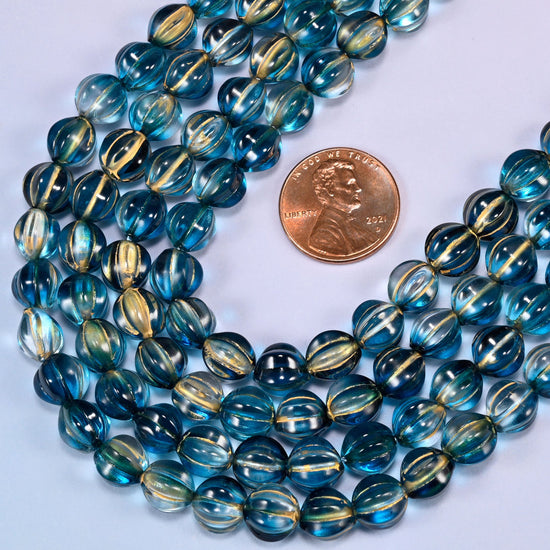 Dark blue gold pumpkin glass beads coiled loosely, shown with a US penny resting on the strands for scale.