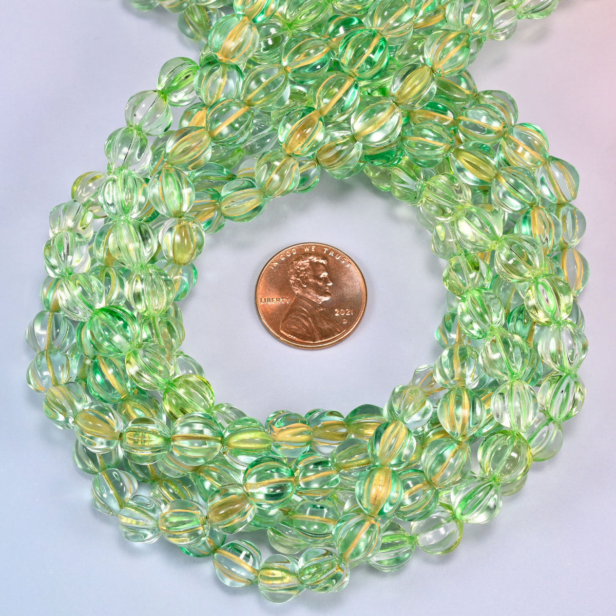 Green gold pumpkin glass beads coiled tightly, shown with a US penny in the open center for scale.