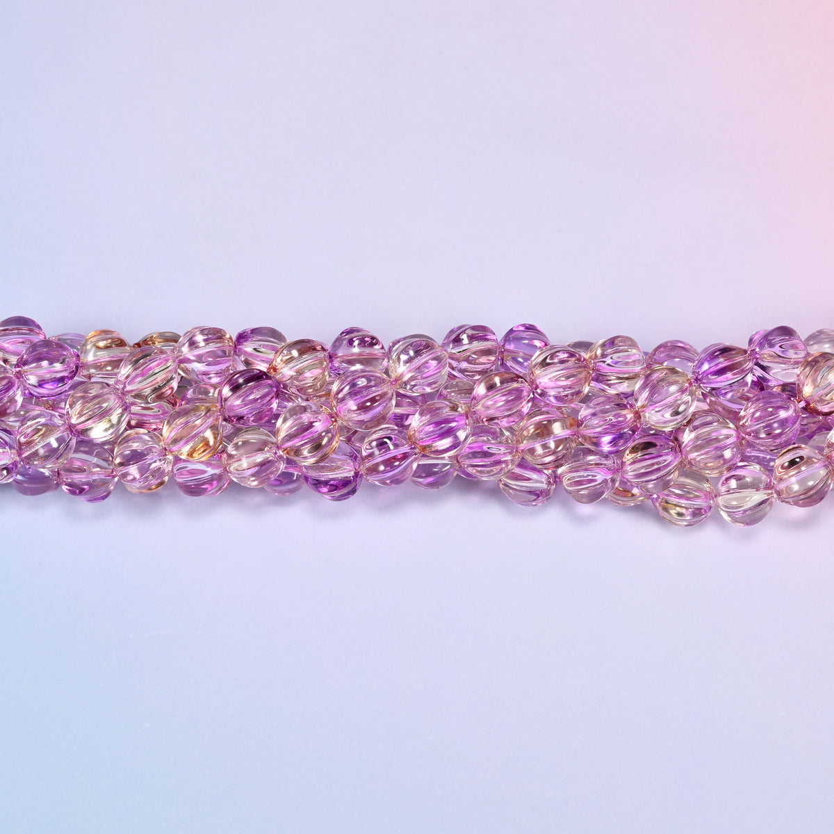 Clear purple gold pumpkin glass beads, 8mm melon rounds, strands laid in a gentle wave straight across the frame.