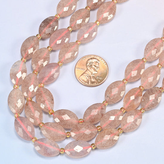 Close view of strawberry quartz faceted flat oval strands curving beside a US penny for scale