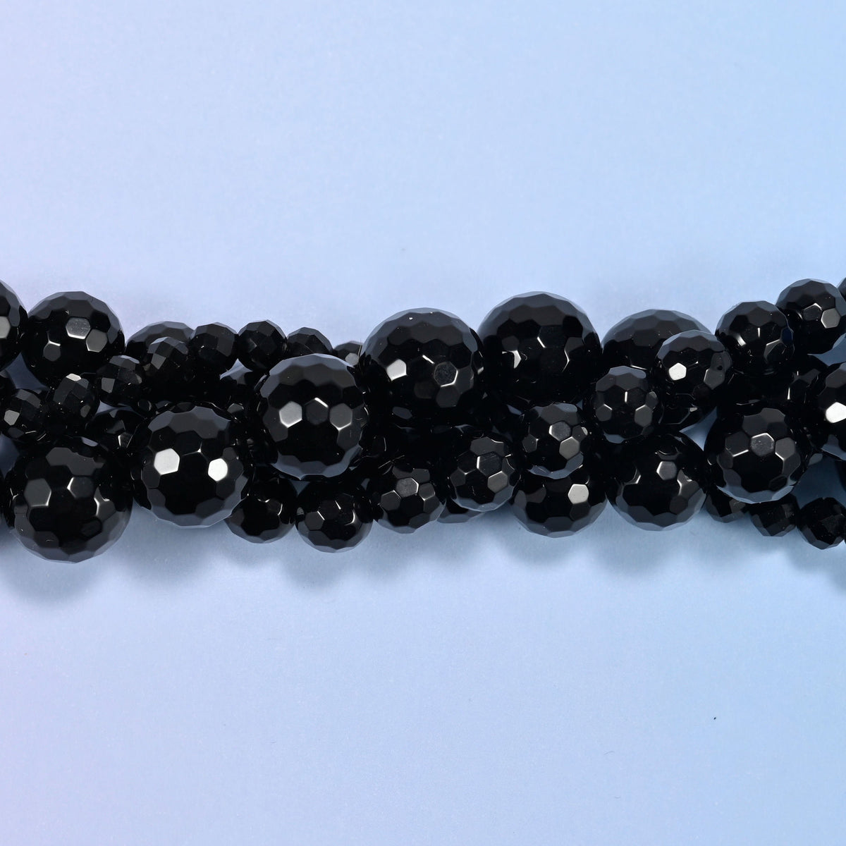 Close view of black onyx faceted round beads, two strands crossing with facets catching light.
