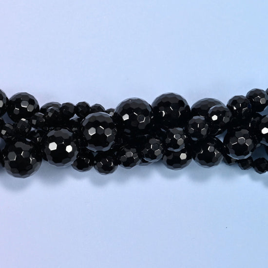 Close view of black onyx faceted round beads, two strands crossing with facets catching light.