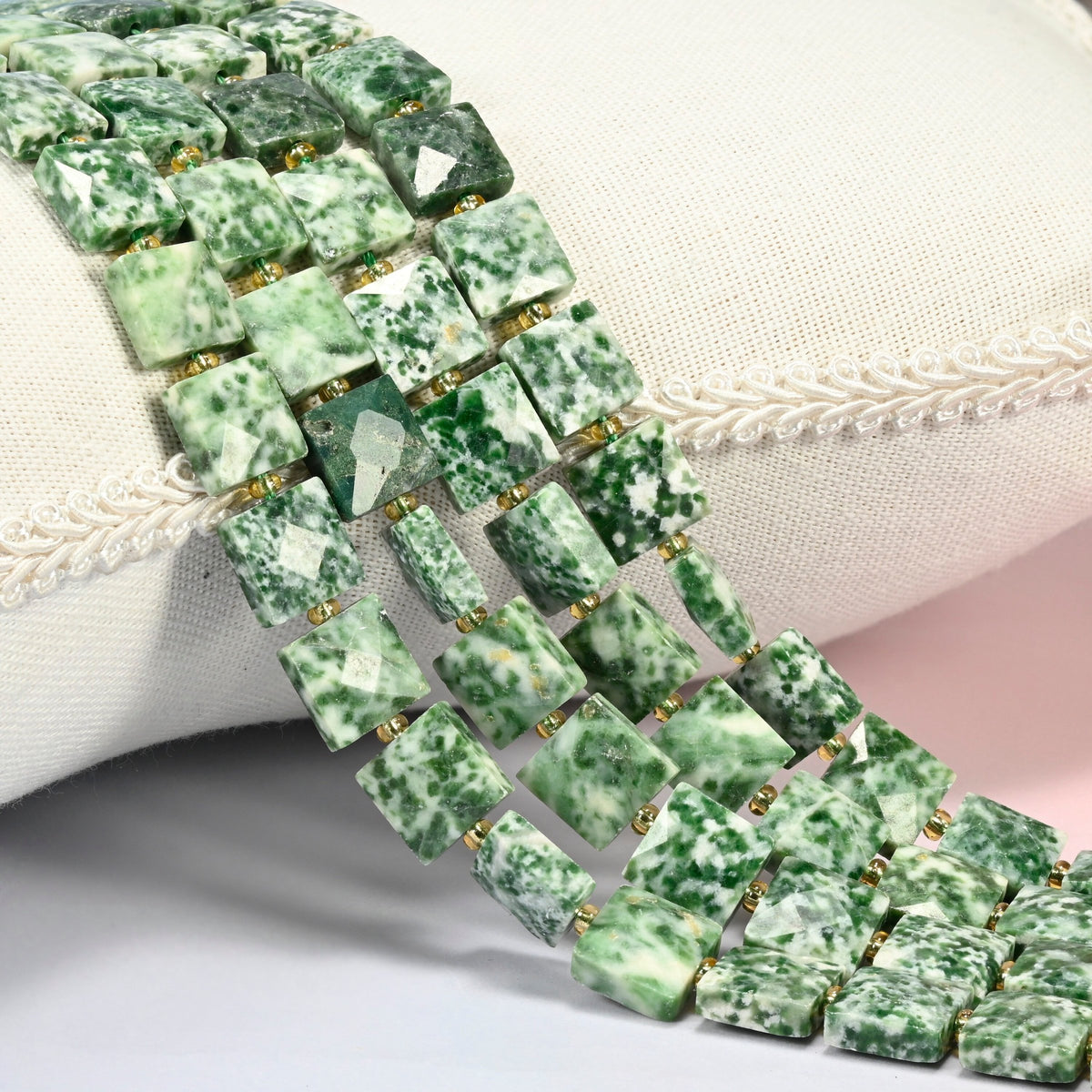 Tree agate faceted flat square beads 10x10mm with small gold seed bead spacers, several strands draped over a white cushion