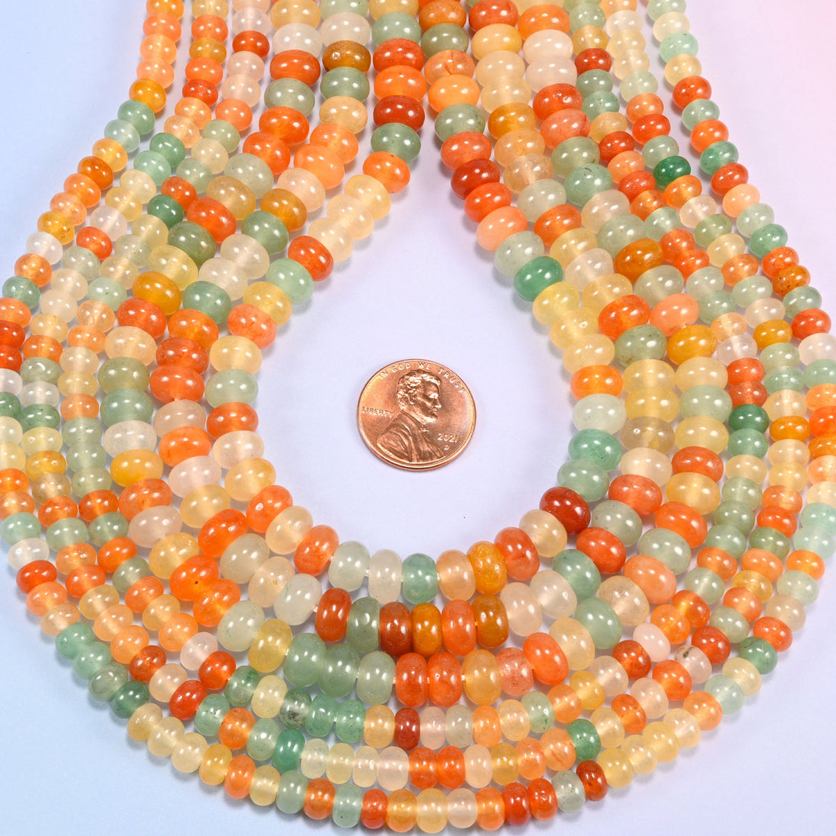 Gold Silk Jade gemstone rondelle beads in a teardrop coil, warm orange and cream discs stacked close together
