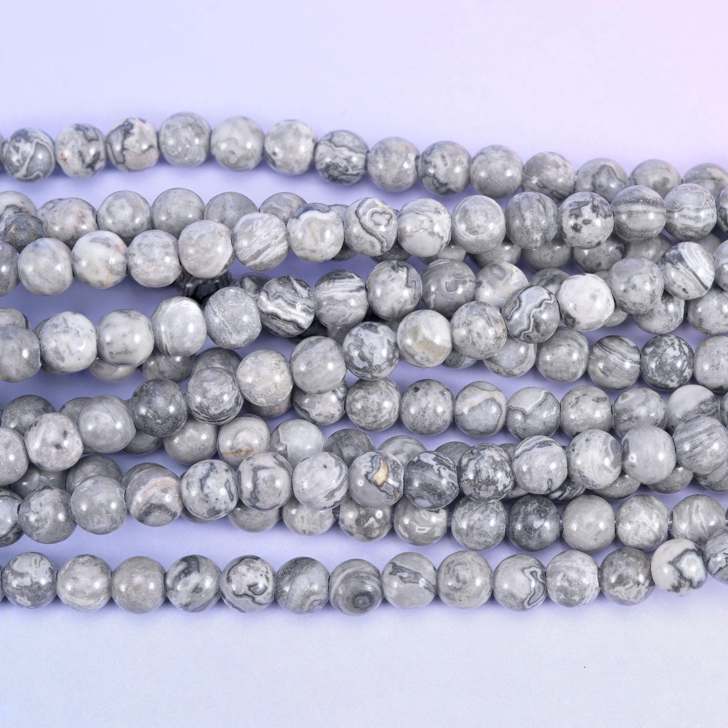 Pale dove grey mapped over with darker charcoal veining, these rounds look like miniature aerial photographs, each bead carrying its own network of thin dark lines across an off-white ground.