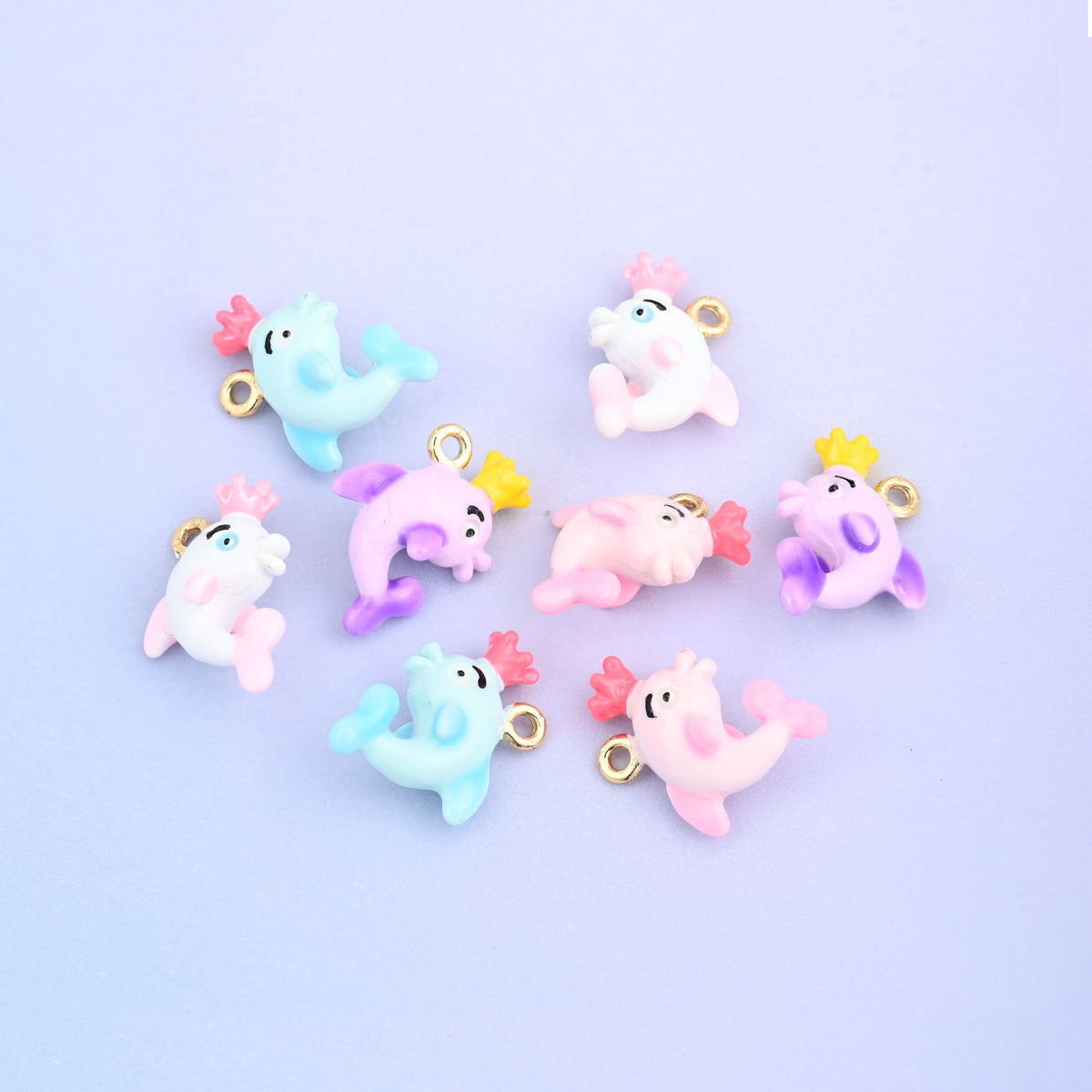 Eight dolphin charms with crowns scattered together, enamel in light blue, white, pink and light purple.