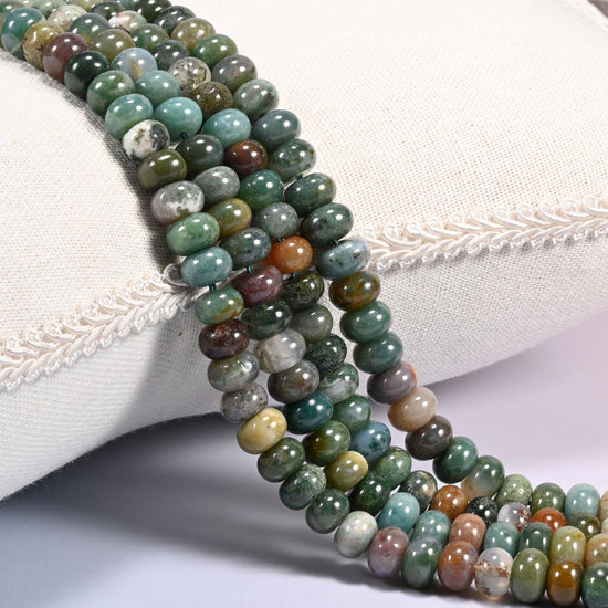 Close-up of multiple strands of polished Indian Agate rondelle beads in green, orange, and cream tones, draped over a cream fabric jewelry display bust.