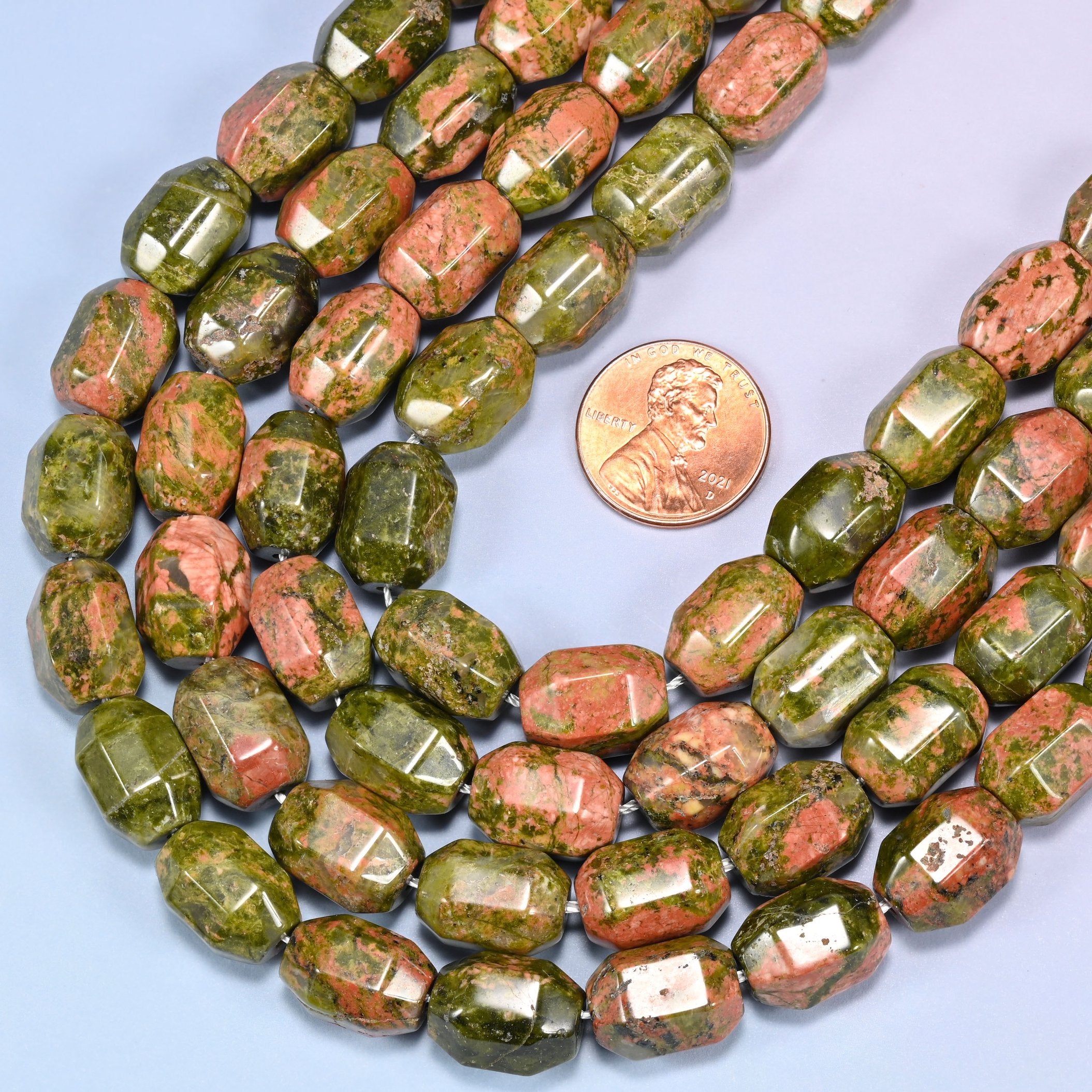 Wide circular coil of faceted Unakite barrel bead strands on a light blue background with a penny in the center for size comparison.