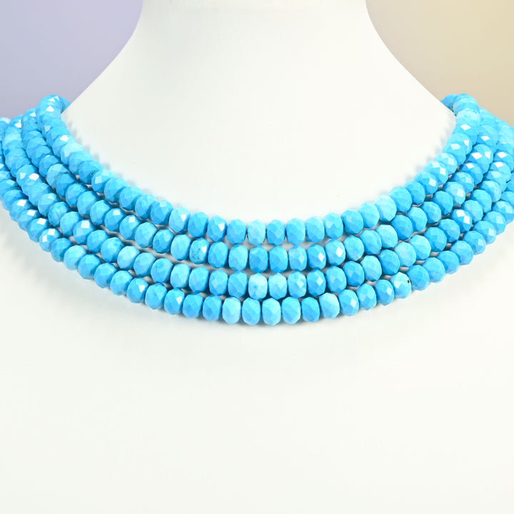Dyed blue howlite faceted rondelle beads on a white neck display, four strands around the bust.