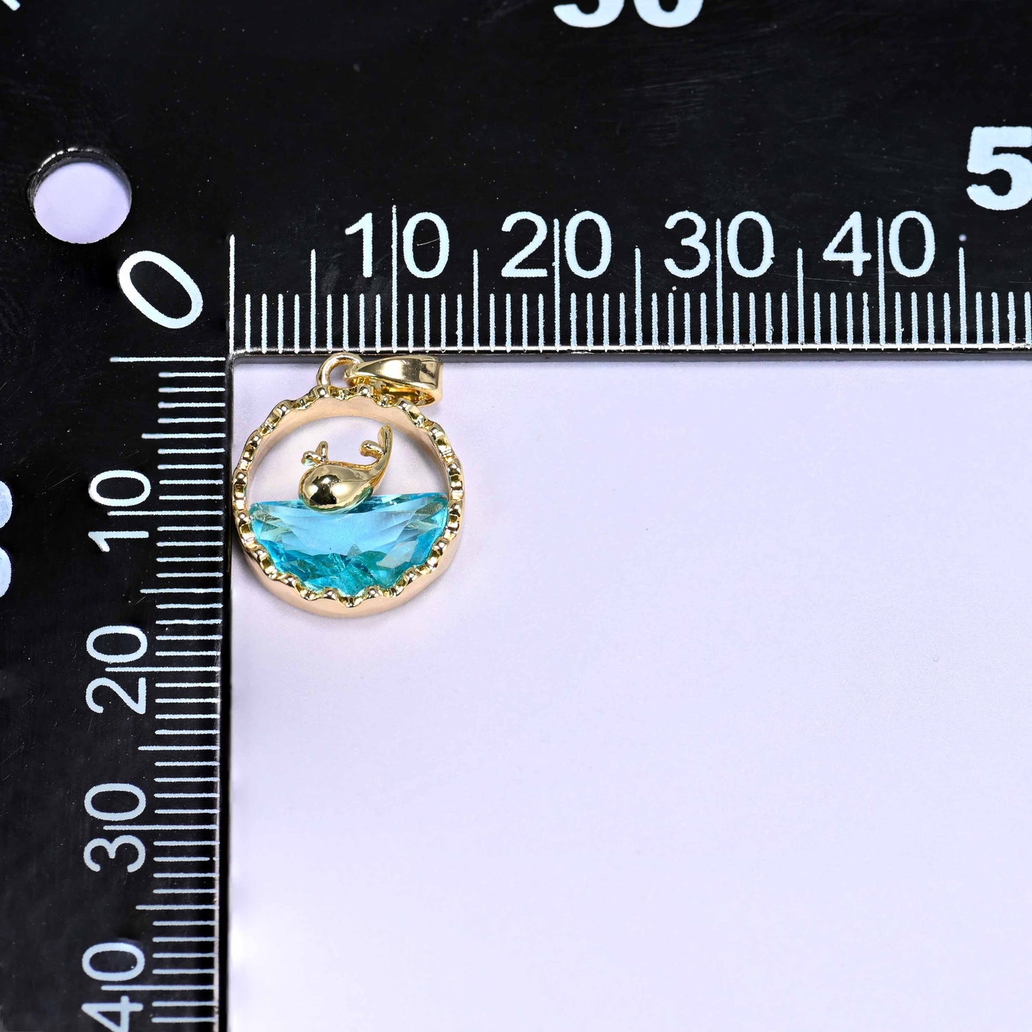 18K gold plated brass whale charm pendant with a gold whale silhouette diving into a faceted blue zirconia wave, set in a textured round frame.