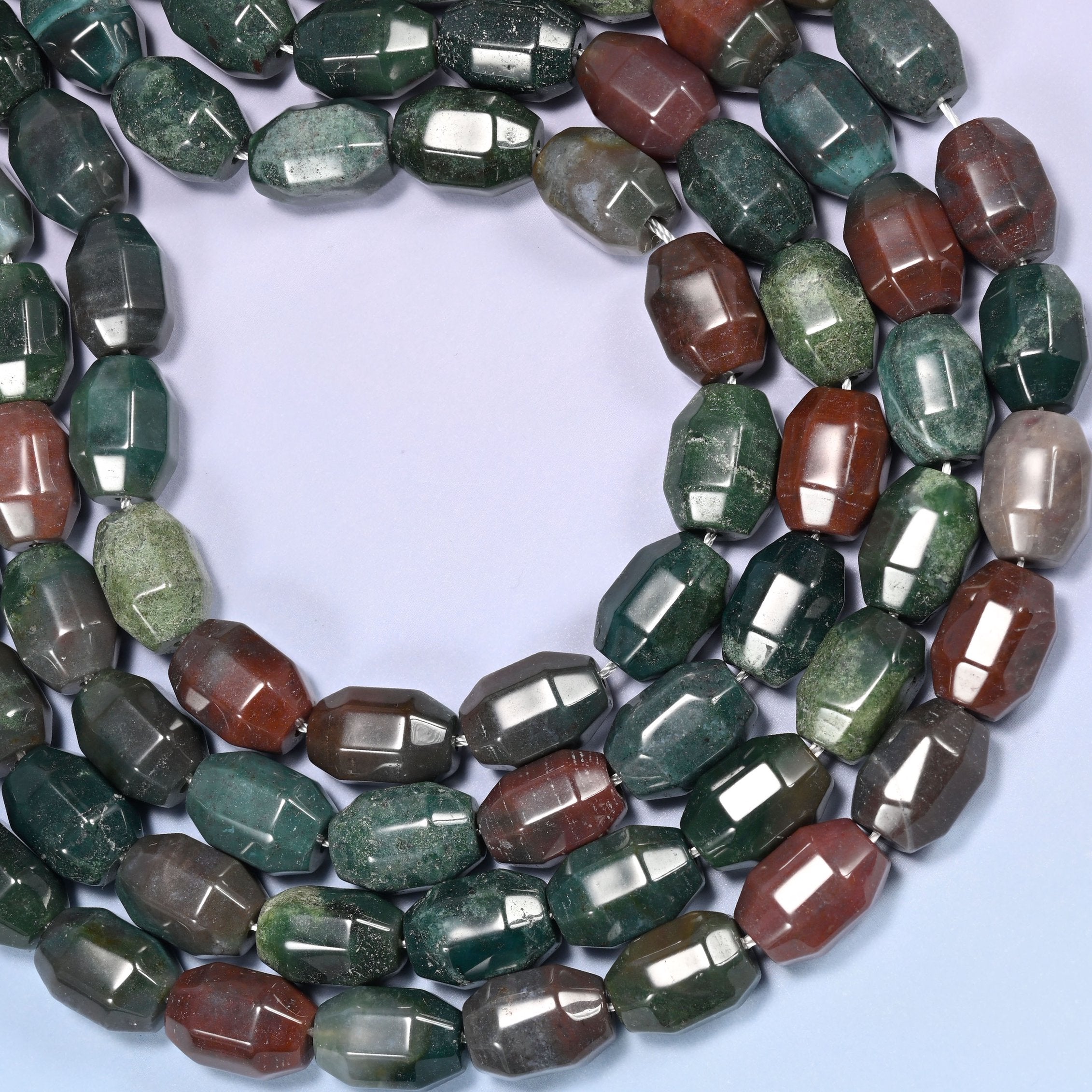Wide circular coil of Indian Agate faceted barrel bead strands on a light lavender background with a penny in the center for size comparison.