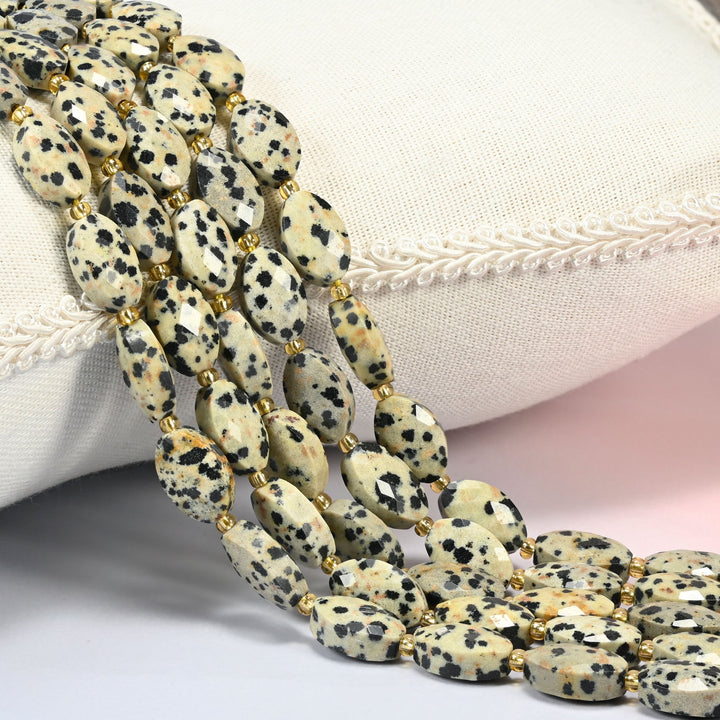 Dalmatian jasper faceted flat oval beads 9x14mm with small gold seed bead spacers, several strands draped over a white cushion