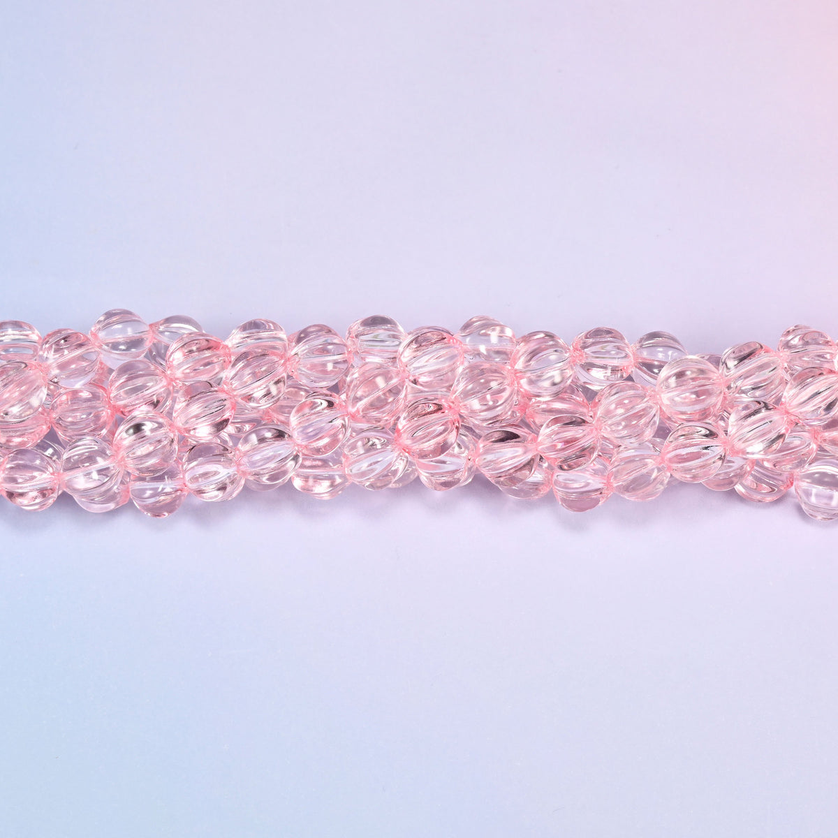 Clear pink pumpkin glass beads coiled loosely, shown with a US penny resting on the strands for scale.