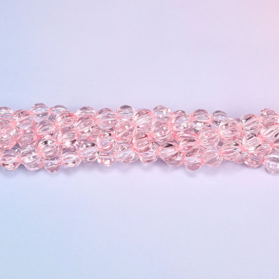 Clear pink pumpkin glass beads coiled loosely, shown with a US penny resting on the strands for scale.