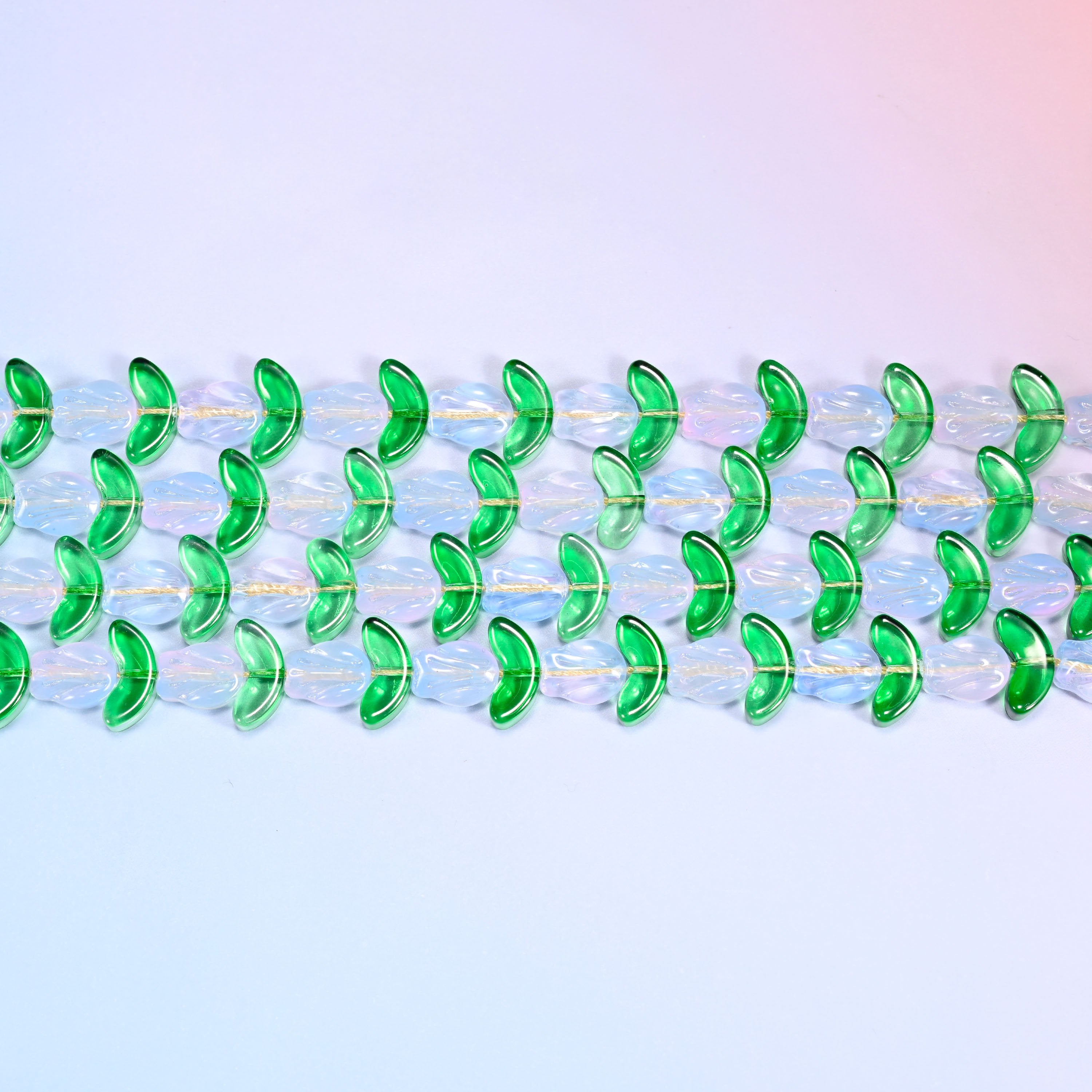 Close-up macro view of white tulip and green leaf glass beads in a dense repeating chevron pattern on a lavender and pink gradient background.