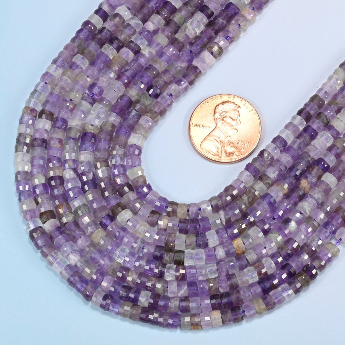 Close view of amethyst faceted heishi disc strands curving beside a US penny for scale