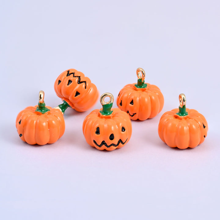 A group of five enamel pumpkin charms in orange with green stems and gold-tone rings, some turned to show the jack o lantern face and some the plain ribbed back.