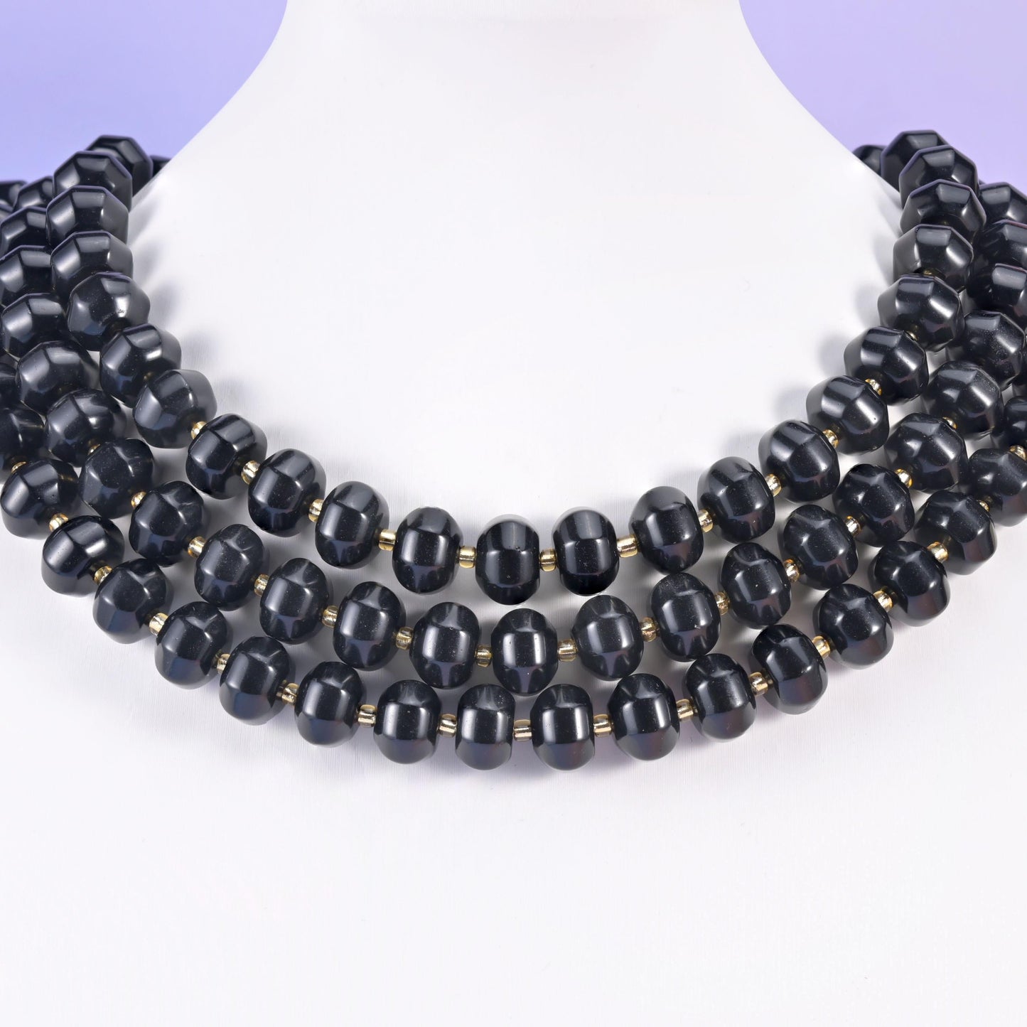 Multi-strand pumpkin rondelle necklace on a white display bust, deep black grooved beads at the collarbone