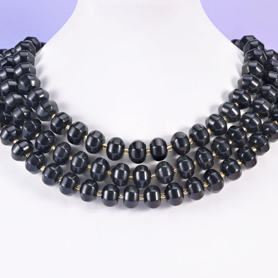 Multi-strand pumpkin rondelle necklace on a white display bust, deep black grooved beads at the collarbone