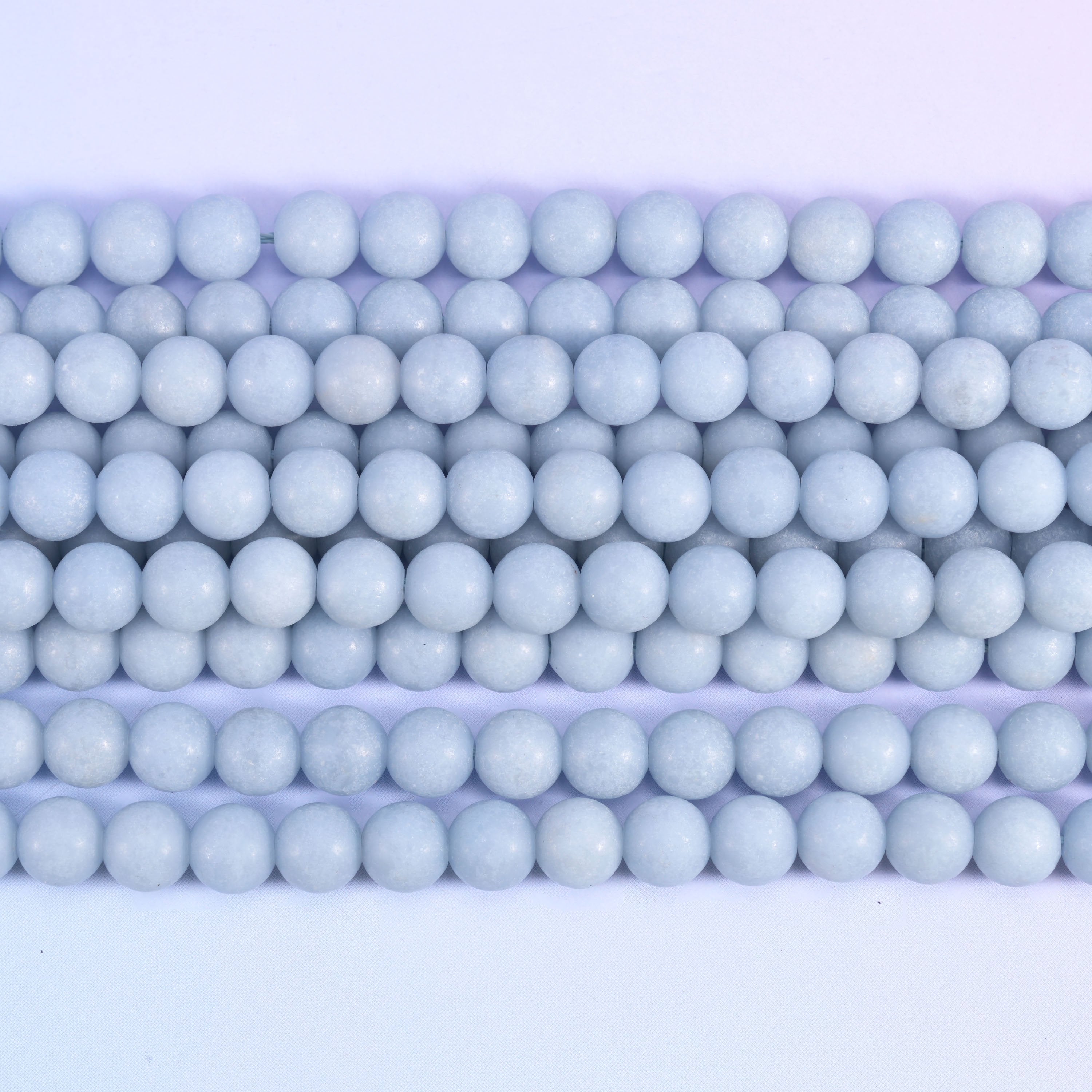 Pale powder blue rounds with a soft matte surface — no shine, no strong veining, just an even chalky sky blue running the length of the strand. One of the calmest, most consistent pastels in the shop.