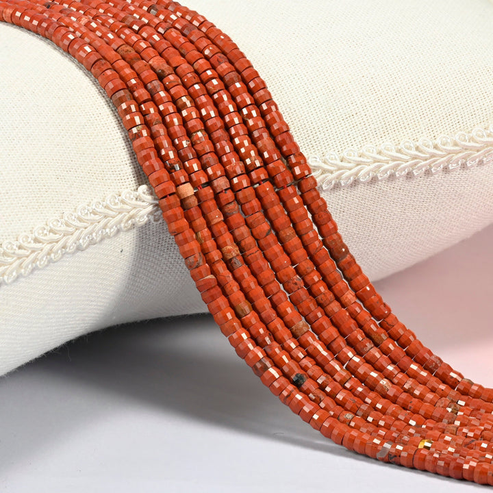 Red jasper faceted heishi disc beads 2x4mm, several strands draped over a white cushion
