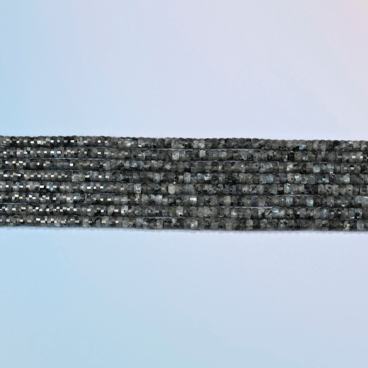 Several strands of black labradorite faceted heishi disc beads laid in straight rows