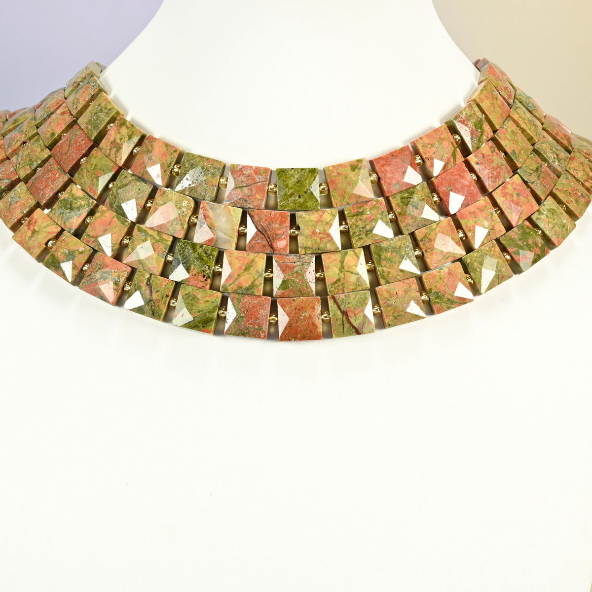 Natural unakite faceted flat square strands arranged as a layered collar on a white display bust, green and pink beads across the neck