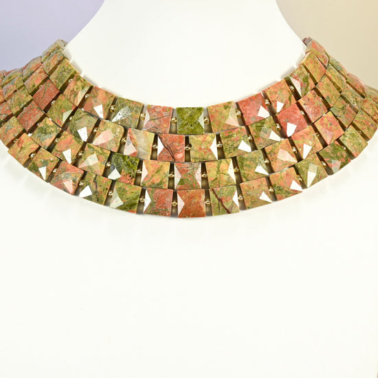 Natural unakite faceted flat square strands arranged as a layered collar on a white display bust, green and pink beads across the neck