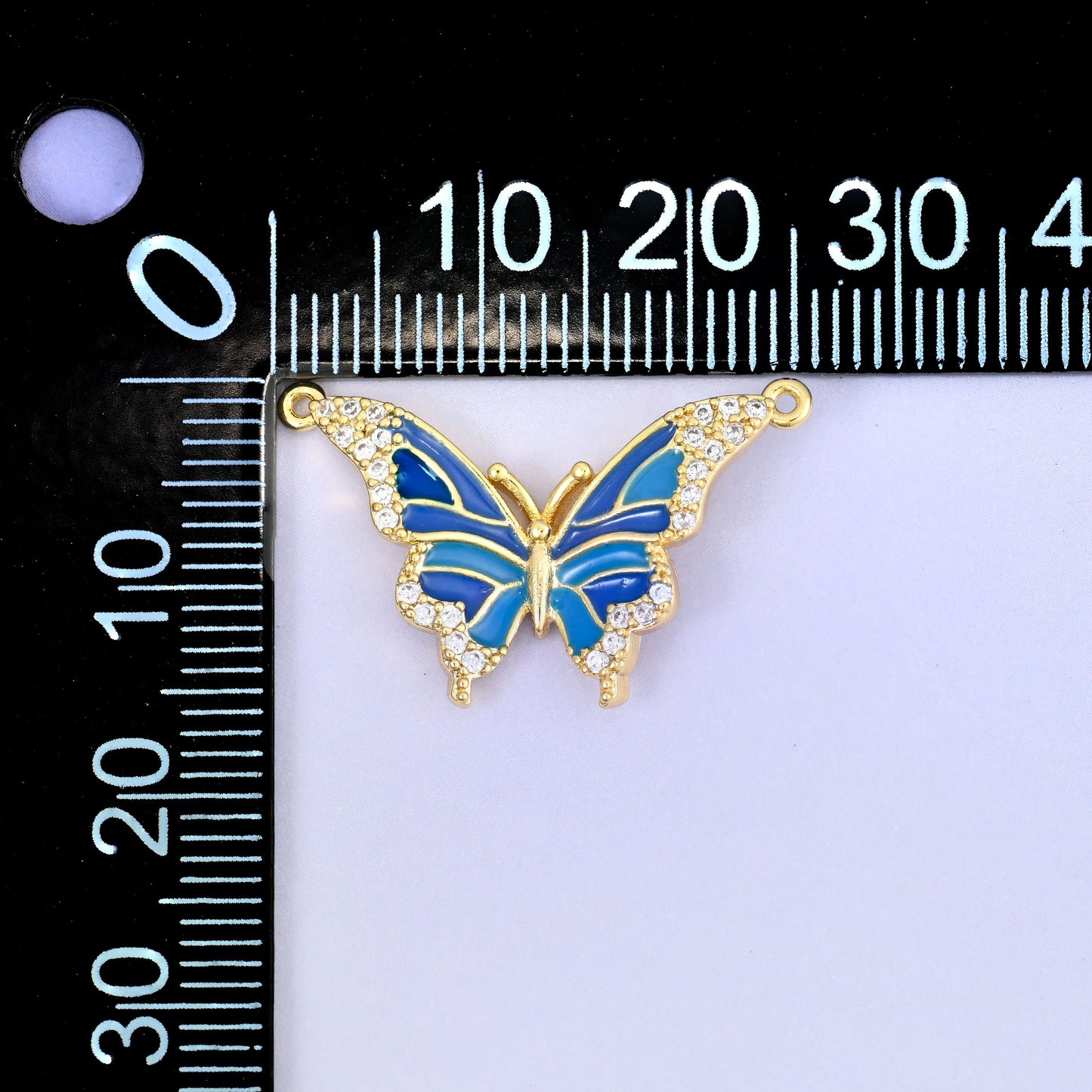 Enamel butterfly double connector pendant measured against a black millimetre ruler, the blue charm laid across the scale to show its wingspan.