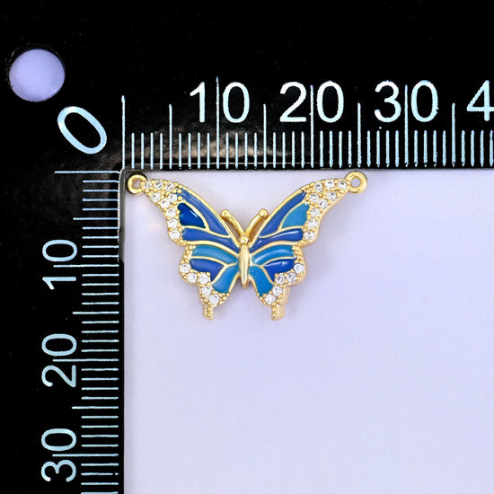 Enamel butterfly double connector pendant measured against a black millimetre ruler, the blue charm laid across the scale to show its wingspan.