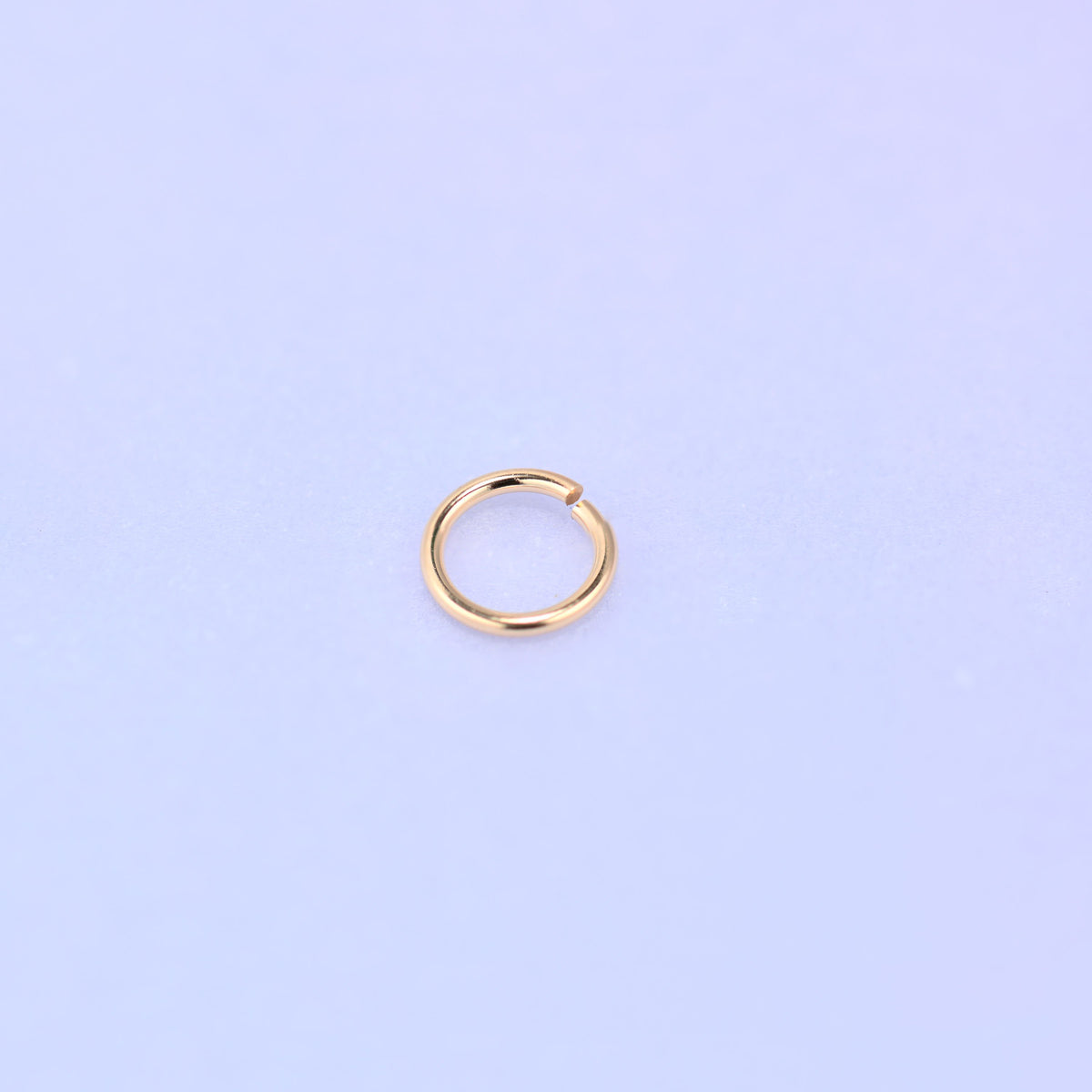 One 14K gold filled open jump ring tilted slightly toward the camera, the polished 0.64mm wire catching the light along the upper curve.