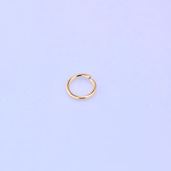 One 14K gold filled open jump ring tilted slightly toward the camera, the polished 0.64mm wire catching the light along the upper curve.