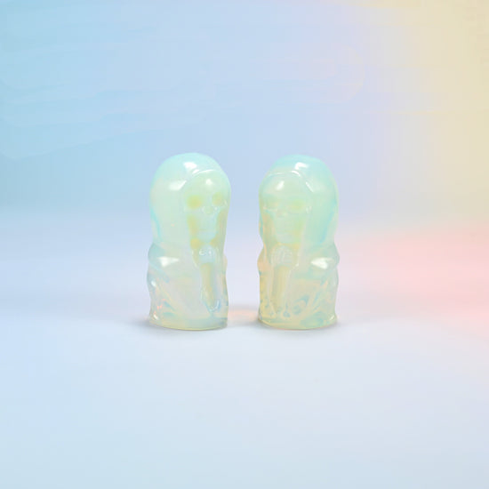 Two opalite hooded skull carvings with a milky glow and a soft blue sheen, man-made glass