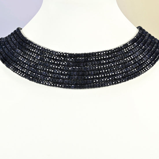 Blue sandstone faceted heishi disc strands arranged as a layered collar on a white display bust, dark blue beads across the neck