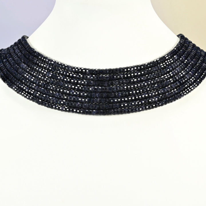 Blue sandstone faceted heishi disc strands arranged as a layered collar on a white display bust, dark blue beads across the neck