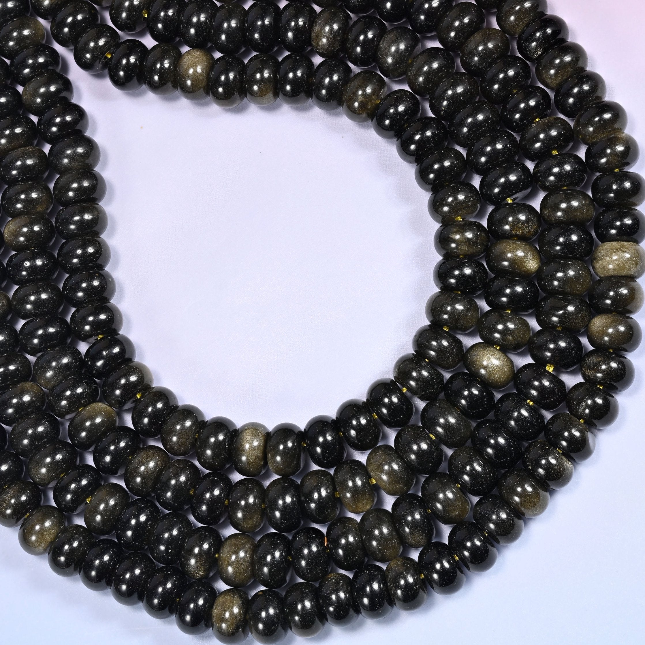 Circular coil of Gold Obsidian bead strands on a lavender background with a penny in the center for size comparison.