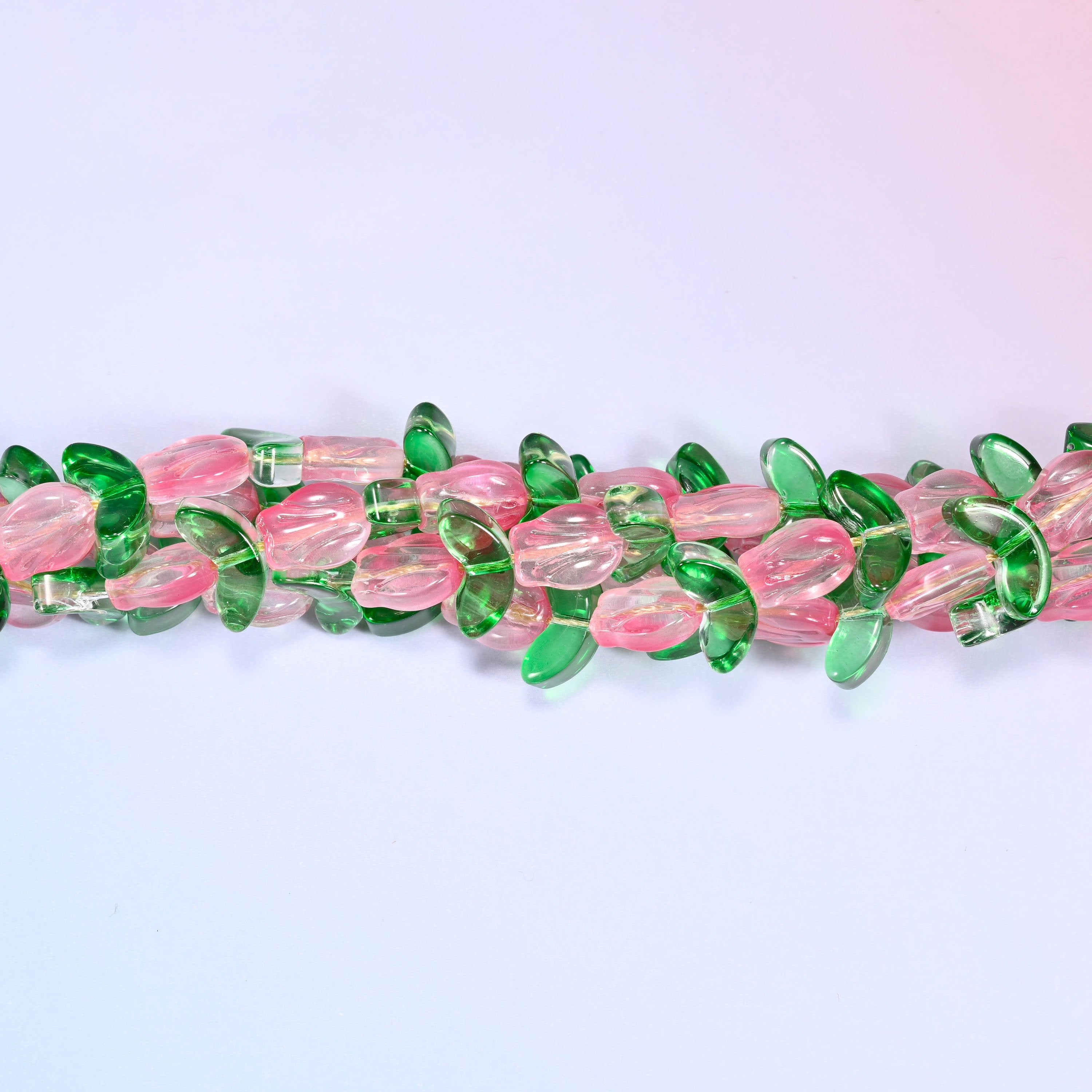 Wide view of a circular coil of pink tulip and green leaf glass bead strands on a lavender and pink gradient background.