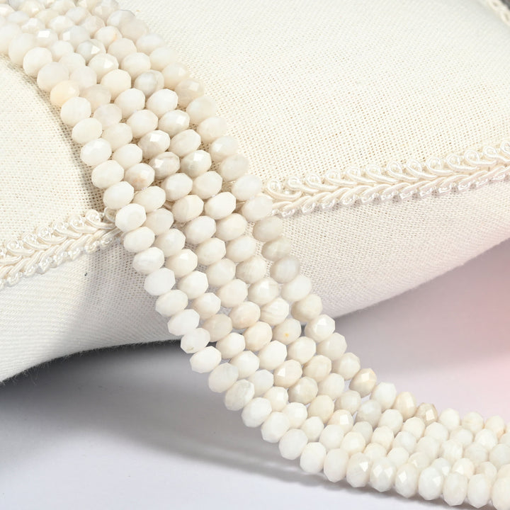 White Crazy Agate gemstone rondelle beads 4x6mm faceted, strand draped over a cream fabric cushion