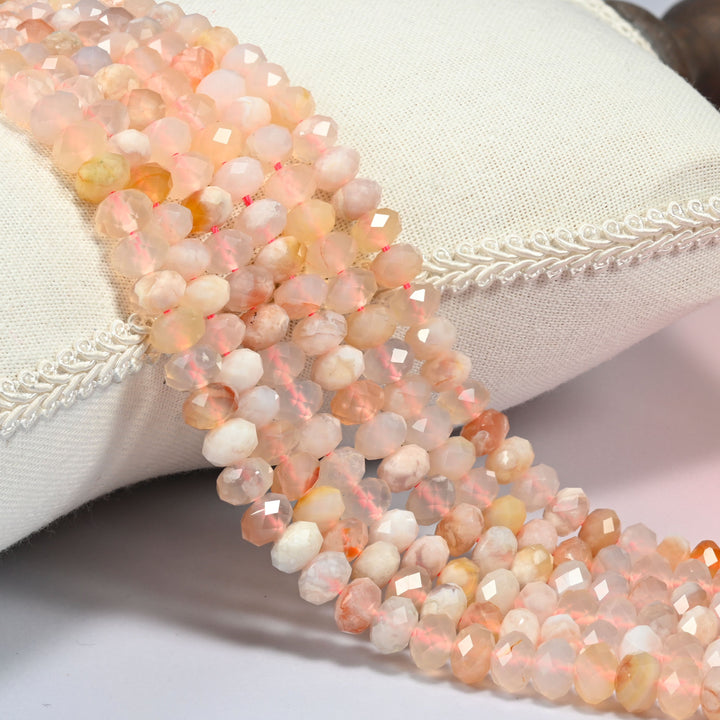 Sakura flower agate faceted rondelle beads 5x8mm in light pink, cream and light orange, several strands draped over a white cushion
