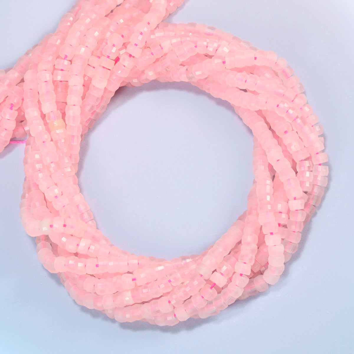 Rose quartz faceted heishi disc beads coiled into overlapping loops, whole strands of soft pink stone
