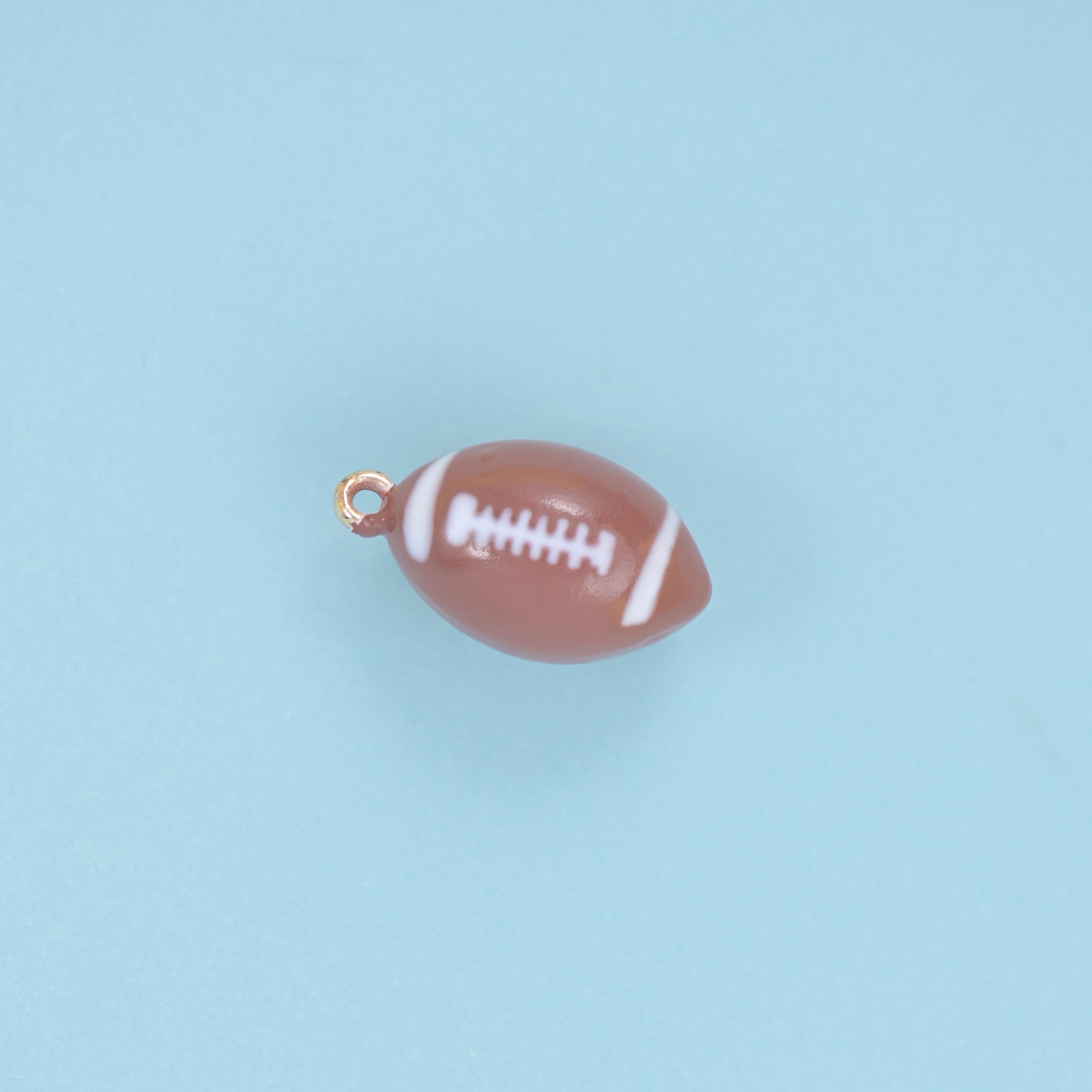 A fully rounded miniature football in glossy warm brown enamel with crisp white lacing and side stripes