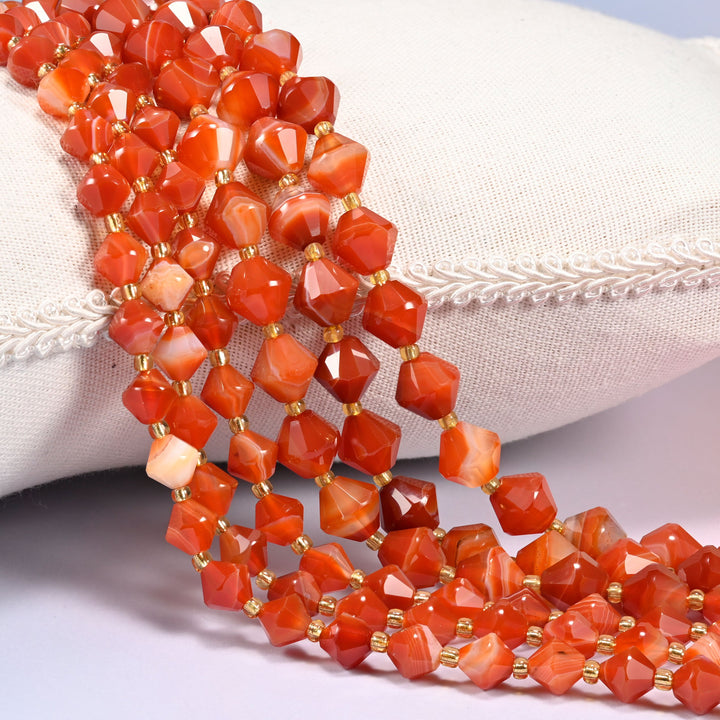 Dyed Red Strip Agate faceted bicone beads draped over a cushion, close-up of the red color and gold-tone spacers.