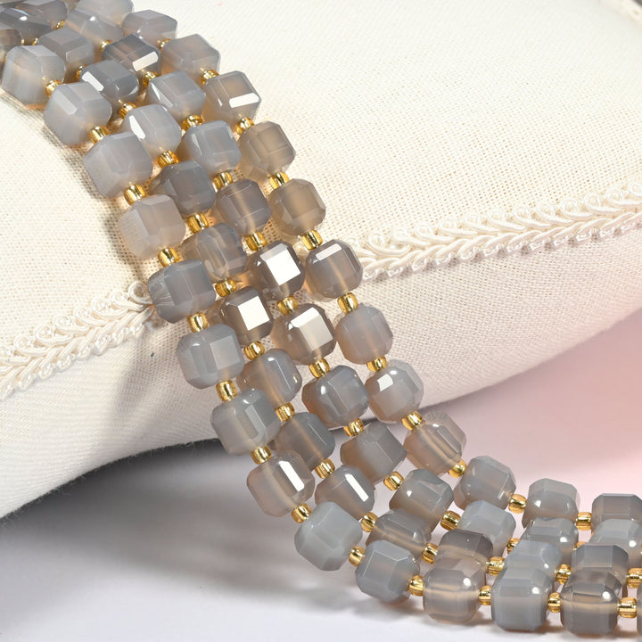 Gray agate faceted cube beads 8mm with small gold spacer beads, several strands draped over a white cushion